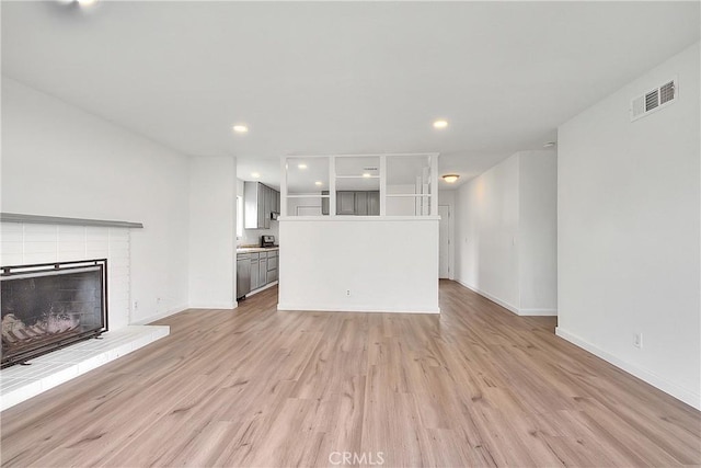 unfurnished living room featuring a brick fireplace, visible vents, light wood-type flooring, and baseboards