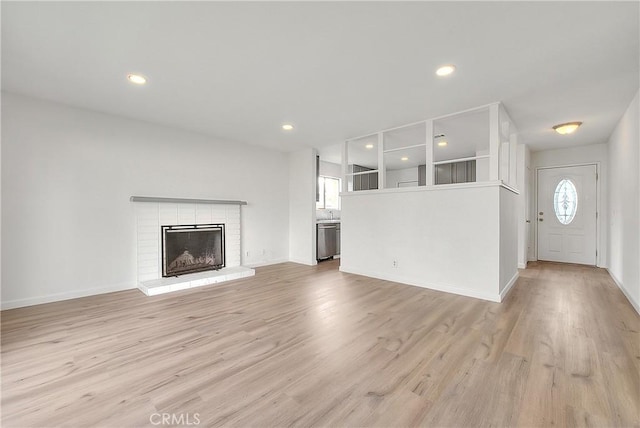 unfurnished living room with a brick fireplace, light wood-style flooring, recessed lighting, and a wealth of natural light