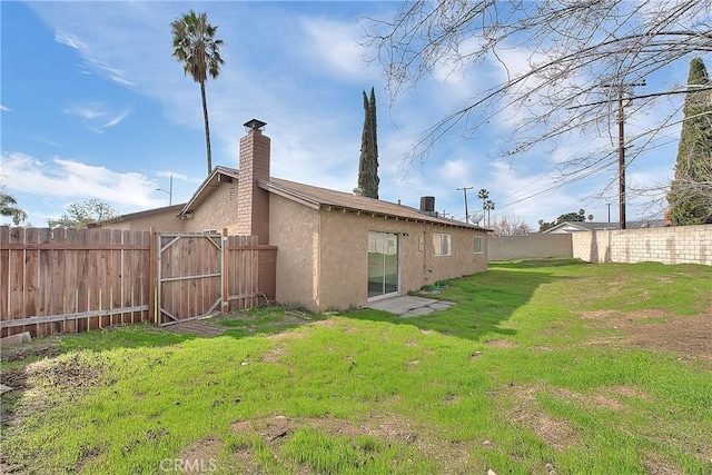 rear view of house with a lawn, a chimney, a fenced backyard, and stucco siding