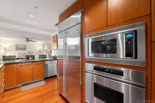 kitchen featuring light wood-type flooring, ceiling fan, sink, built in appliances, and dark stone countertops