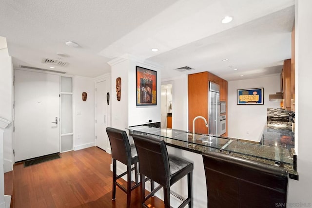 kitchen featuring a breakfast bar, exhaust hood, built in appliances, light wood-type flooring, and kitchen peninsula