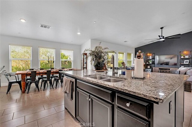 kitchen featuring light stone countertops, stainless steel dishwasher, vaulted ceiling, a kitchen island with sink, and sink