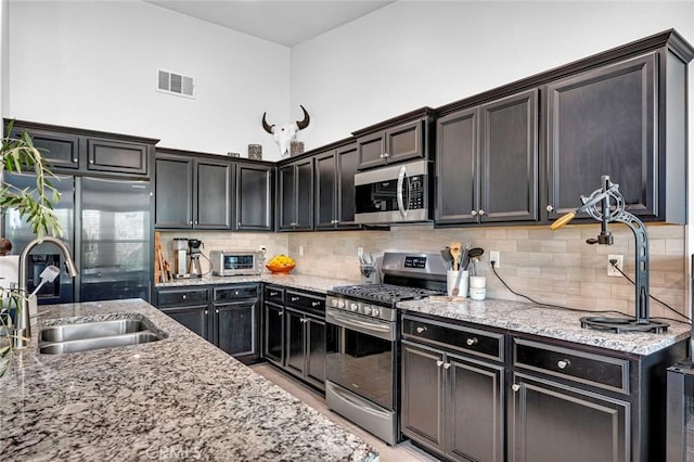 kitchen with backsplash, sink, light stone countertops, a towering ceiling, and stainless steel appliances