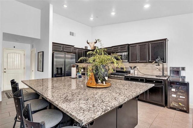 kitchen featuring wine cooler, a kitchen island, light stone counters, dark brown cabinetry, and stainless steel appliances