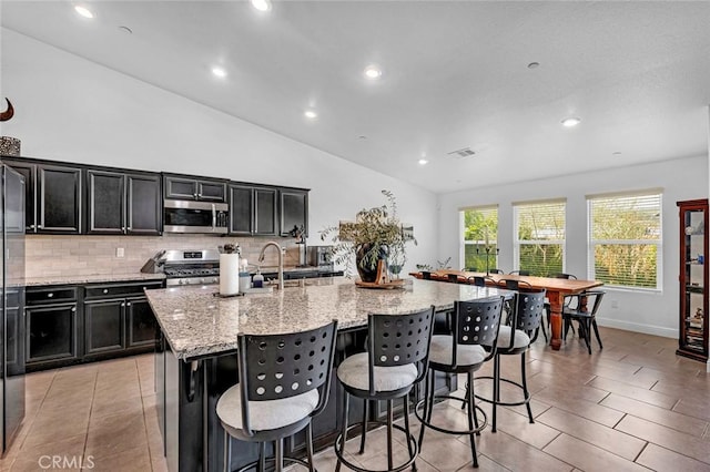 kitchen featuring a kitchen breakfast bar, a kitchen island with sink, vaulted ceiling, and appliances with stainless steel finishes