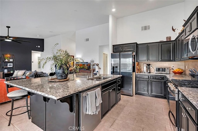 kitchen featuring sink, a kitchen breakfast bar, high vaulted ceiling, a center island with sink, and appliances with stainless steel finishes