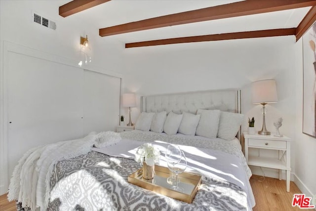 bedroom featuring beamed ceiling and light wood-type flooring