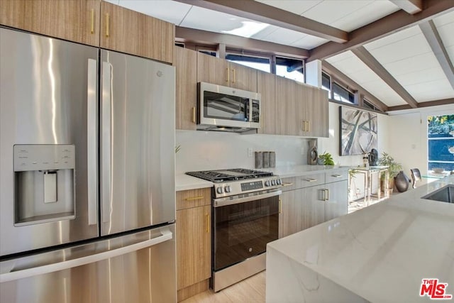 kitchen with light stone countertops, appliances with stainless steel finishes, decorative backsplash, lofted ceiling with beams, and light hardwood / wood-style floors