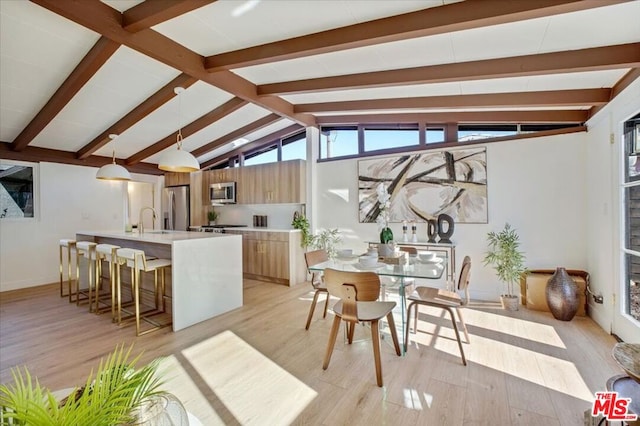 kitchen with vaulted ceiling with beams, decorative light fixtures, appliances with stainless steel finishes, and light hardwood / wood-style flooring