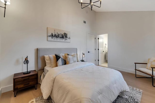 bedroom featuring high vaulted ceiling, hardwood / wood-style floors, a notable chandelier, and ensuite bath