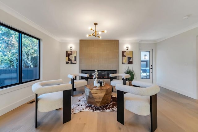 living room featuring crown molding, a fireplace, an inviting chandelier, and light hardwood / wood-style flooring