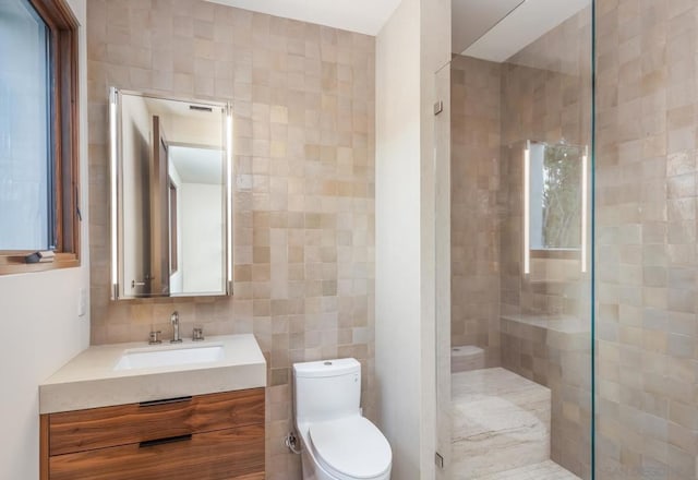 bathroom with vanity, toilet, a shower with door, and tile walls