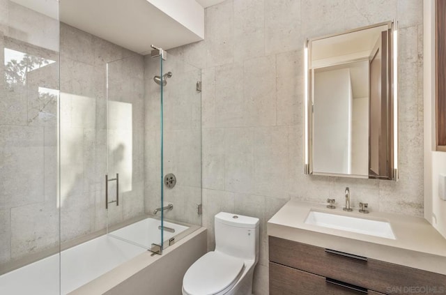 full bathroom featuring vanity, bath / shower combo with glass door, tile walls, and toilet