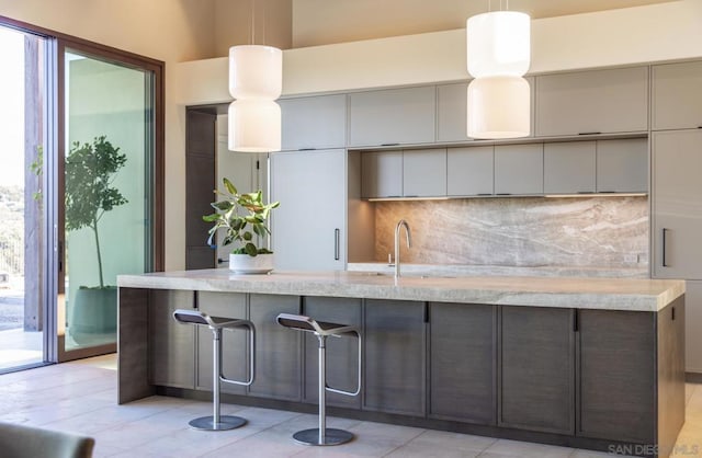 kitchen with a kitchen bar, tasteful backsplash, sink, pendant lighting, and light tile patterned floors