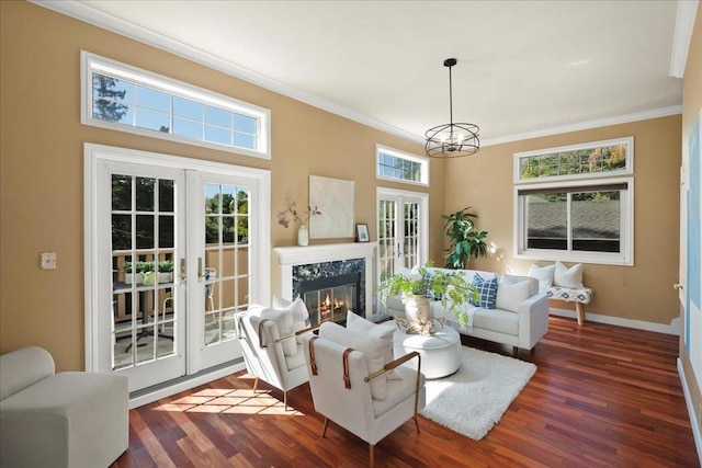 living room featuring dark wood-type flooring, a premium fireplace, french doors, a notable chandelier, and ornamental molding