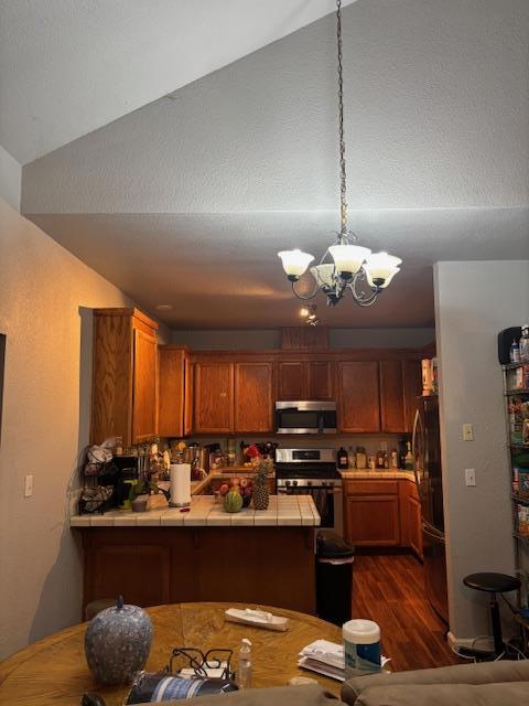 kitchen with tile counters, a chandelier, kitchen peninsula, and stainless steel appliances