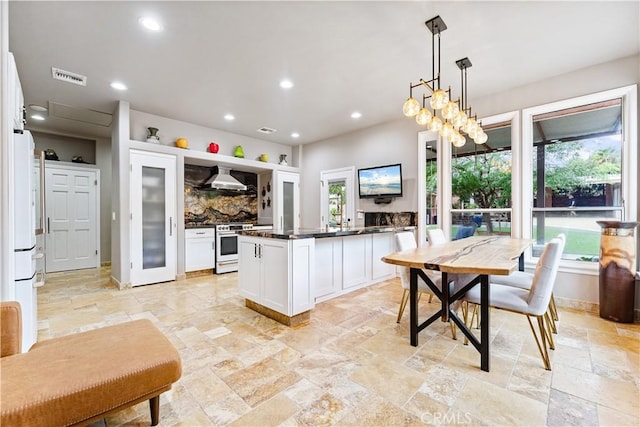 kitchen with a wealth of natural light, white cabinets, pendant lighting, and wall chimney range hood