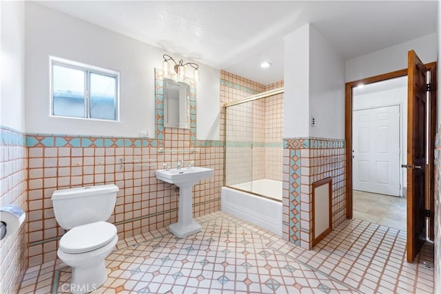 bathroom with tile patterned floors, toilet, enclosed tub / shower combo, and tile walls