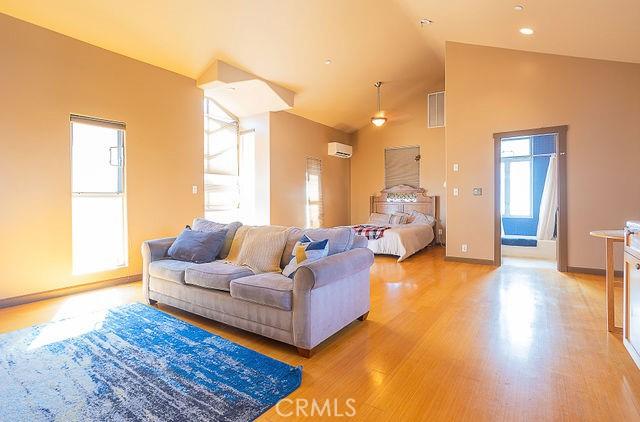 living area featuring baseboards, visible vents, a wall mounted air conditioner, high vaulted ceiling, and light wood finished floors