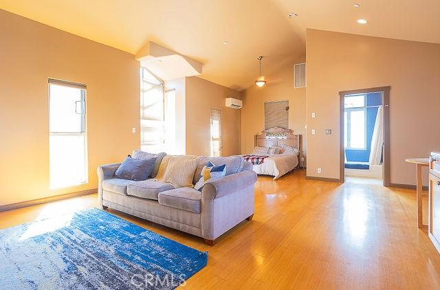 bedroom featuring visible vents, baseboards, light wood-type flooring, an AC wall unit, and high vaulted ceiling
