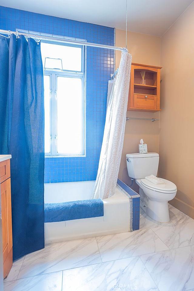 full bathroom with shower / tub combo with curtain, plenty of natural light, toilet, and vanity