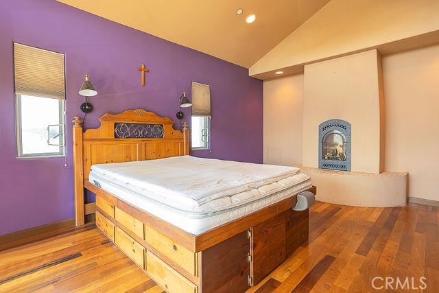 bedroom featuring a large fireplace, light wood finished floors, lofted ceiling, and multiple windows