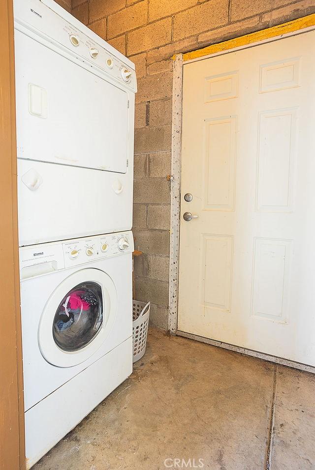 laundry room featuring laundry area, stacked washer / dryer, and concrete block wall