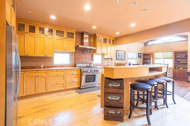 kitchen with a kitchen island, appliances with stainless steel finishes, a breakfast bar, wall chimney range hood, and light hardwood / wood-style flooring