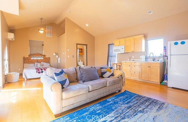 living room featuring visible vents, high vaulted ceiling, an AC wall unit, and light wood-type flooring