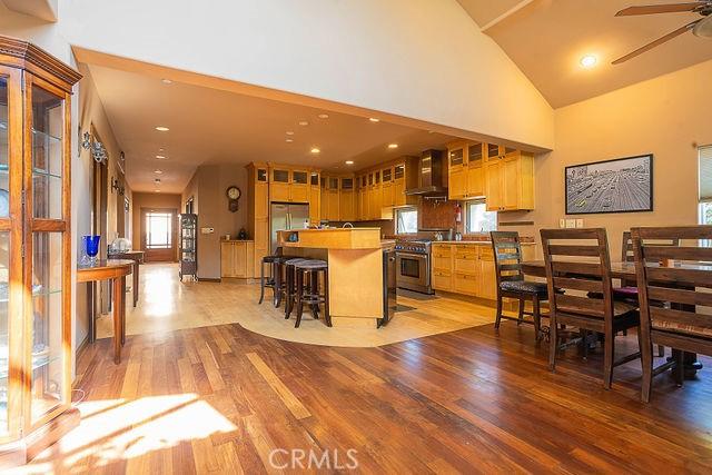 kitchen featuring wall chimney range hood, appliances with stainless steel finishes, light wood finished floors, ceiling fan, and glass insert cabinets