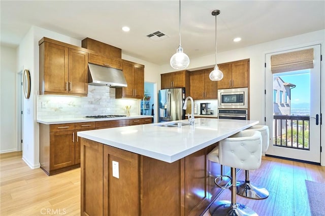 kitchen featuring sink, appliances with stainless steel finishes, a kitchen island with sink, hanging light fixtures, and exhaust hood