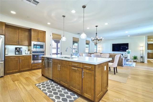 kitchen with sink, a kitchen island with sink, hanging light fixtures, stainless steel appliances, and light wood-type flooring