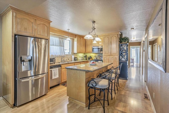 kitchen with a breakfast bar, hanging light fixtures, stainless steel appliances, a center island, and light wood-type flooring