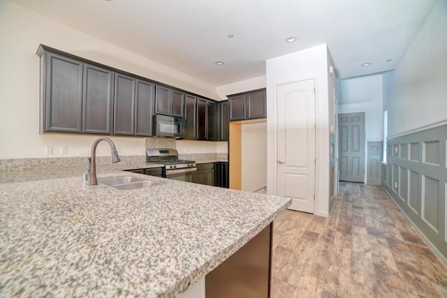 kitchen featuring kitchen peninsula, stainless steel gas range oven, sink, and dark brown cabinets