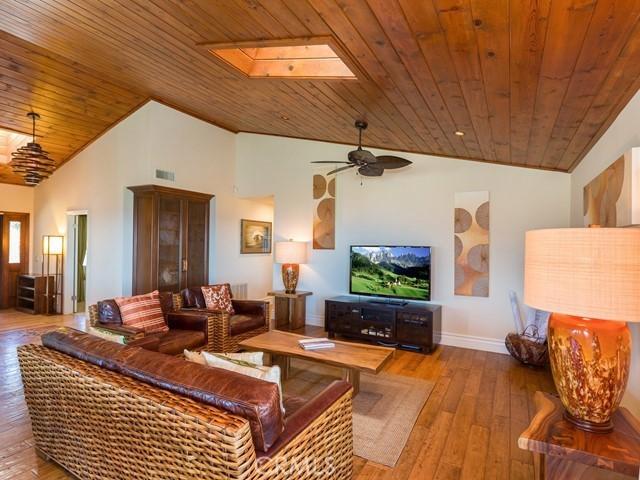 living room with hardwood / wood-style flooring, ceiling fan, vaulted ceiling with skylight, and wooden ceiling