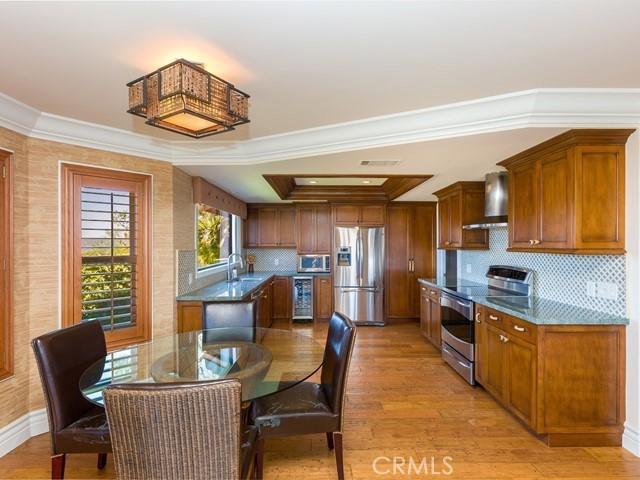 kitchen with ornamental molding, stainless steel appliances, sink, wall chimney range hood, and light hardwood / wood-style floors