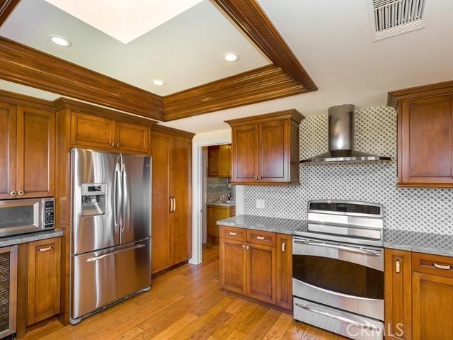 kitchen with decorative backsplash, light hardwood / wood-style floors, wall chimney range hood, and stainless steel appliances