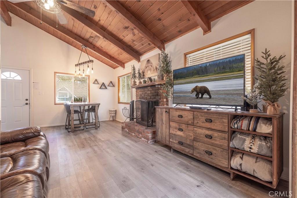 living room featuring beamed ceiling, light hardwood / wood-style floors, a brick fireplace, and wood ceiling