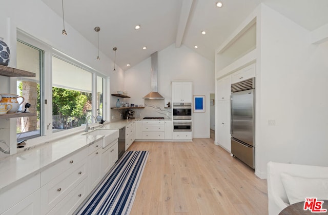 kitchen with white cabinets, wall chimney range hood, sink, light wood-type flooring, and stainless steel appliances