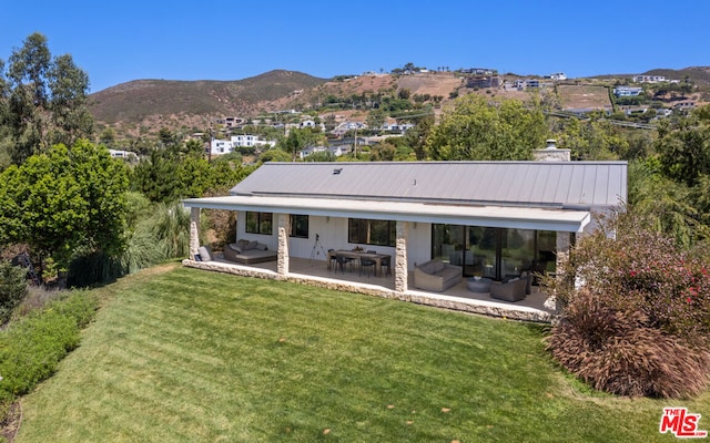 rear view of property featuring a lawn, an outdoor living space, a patio area, and a mountain view