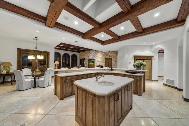 kitchen featuring pendant lighting, an inviting chandelier, sink, an island with sink, and beamed ceiling