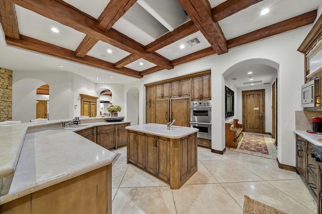 kitchen featuring beam ceiling, sink, built in appliances, a spacious island, and light tile patterned floors