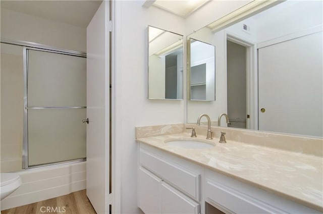 full bathroom featuring hardwood / wood-style flooring, combined bath / shower with glass door, vanity, and toilet