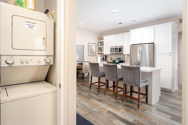 kitchen featuring white cabinetry, stacked washer / dryer, stainless steel appliances, and light hardwood / wood-style flooring