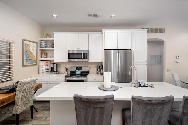 kitchen featuring a kitchen breakfast bar, appliances with stainless steel finishes, a kitchen island with sink, white cabinets, and hardwood / wood-style flooring