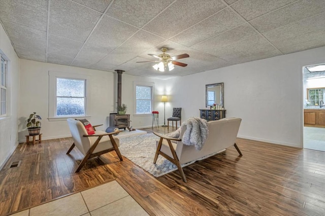 living room with ceiling fan, a wood stove, and hardwood / wood-style floors