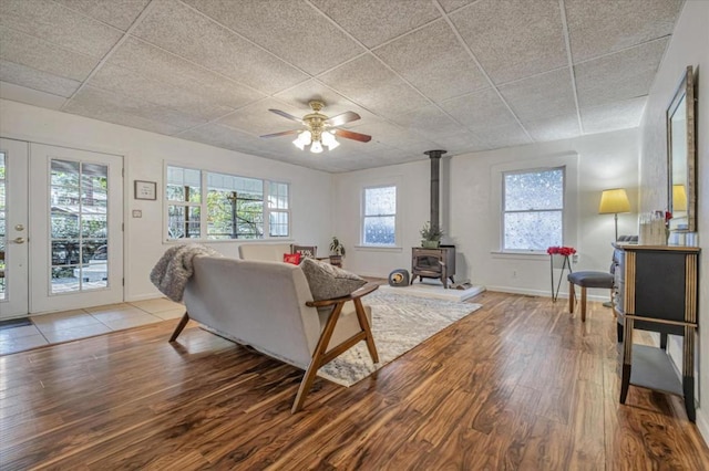 living room with a paneled ceiling, ceiling fan, a wood stove, and wood-type flooring