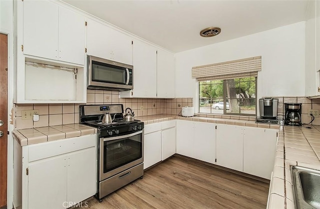 kitchen featuring white cabinets, tile counters, stainless steel appliances, and light hardwood / wood-style flooring