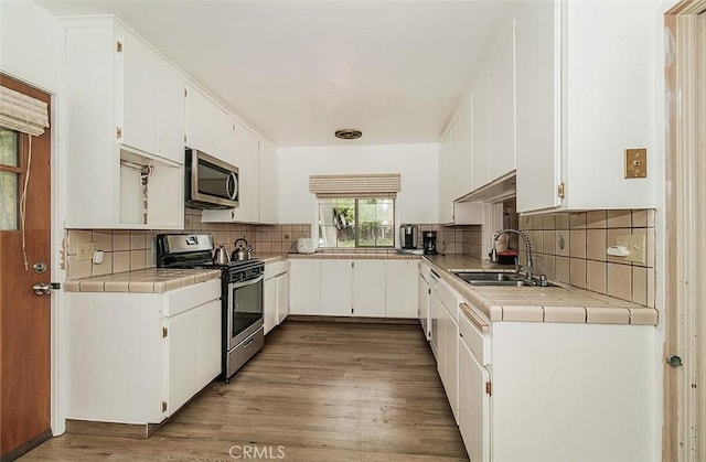 kitchen featuring white cabinetry, sink, tile counters, stainless steel appliances, and light hardwood / wood-style floors