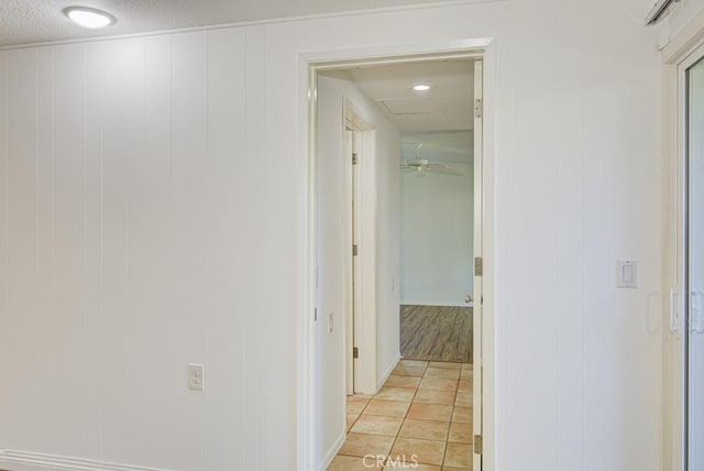 corridor featuring light tile patterned floors, a textured ceiling, and wood walls